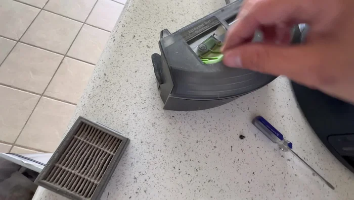 Hauptbürsten reinigen: Mit einem Flachkopf-Schraubendreher die Schraube lösen, den Gummi abziehen, die Bürsten herausnehmen und Haare/Schmutz entfernen. Anschließend wieder zusammenbauen.